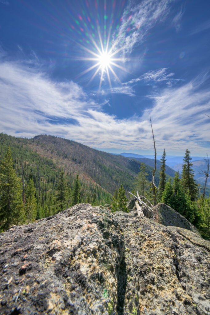 A coarse-grained granite slab in the foreground with a forested drainage falling away behind and distant blue ranges